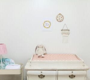 Roze previjalica za bebe sa belim zekom i pelenama na stalku pored.